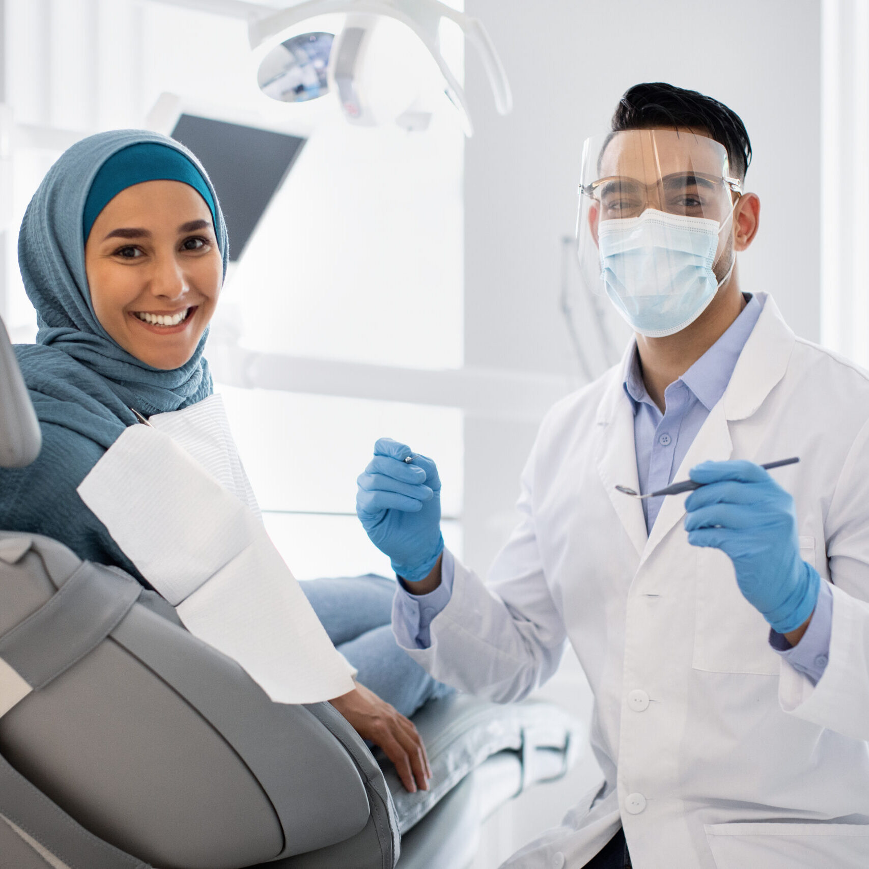 Root Canal Treatment. Stomatologist Man In Medical Mask And Face Shield Having Checkup With Muslim Female Patient In Hijab, Middle Eastern Doctor Holding Dental Tools And Looking At Camera